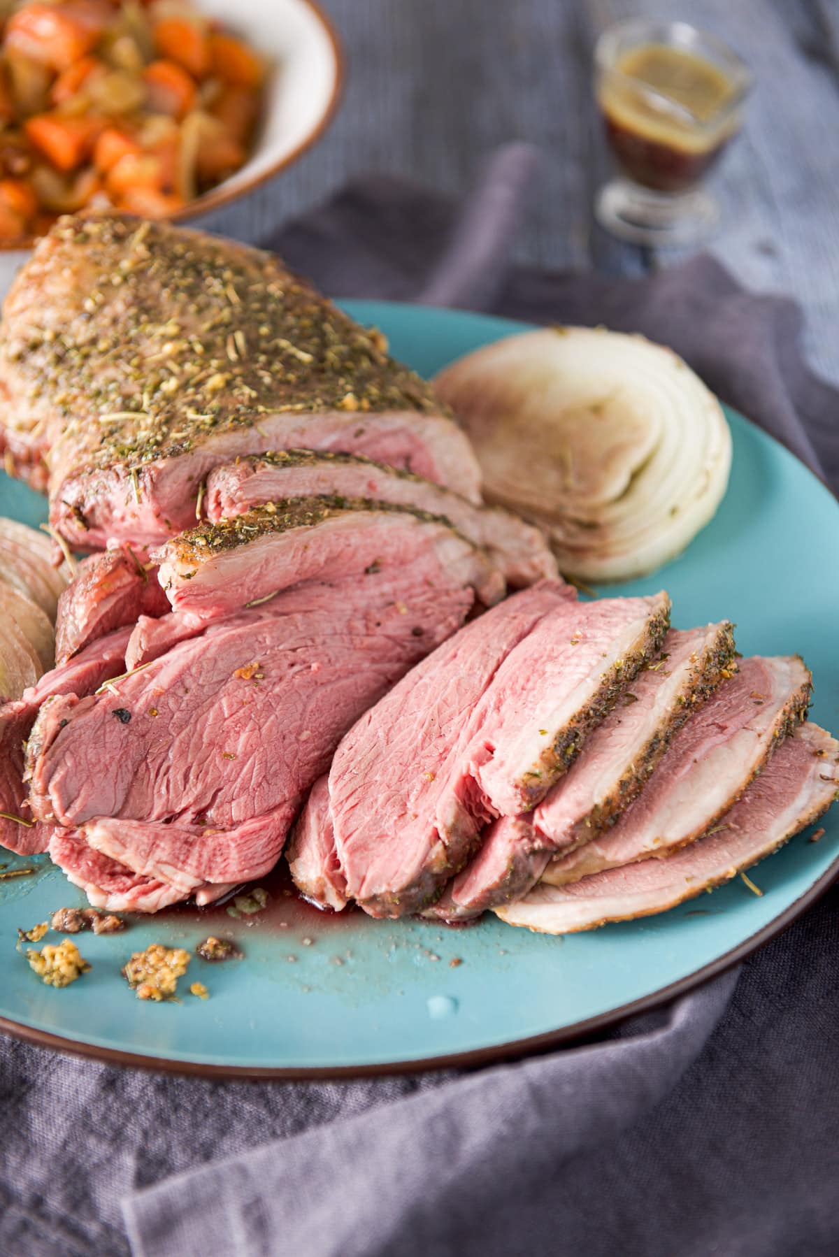 Slices of lamb on a platter with juice in a little pourer and carrots in a bowl