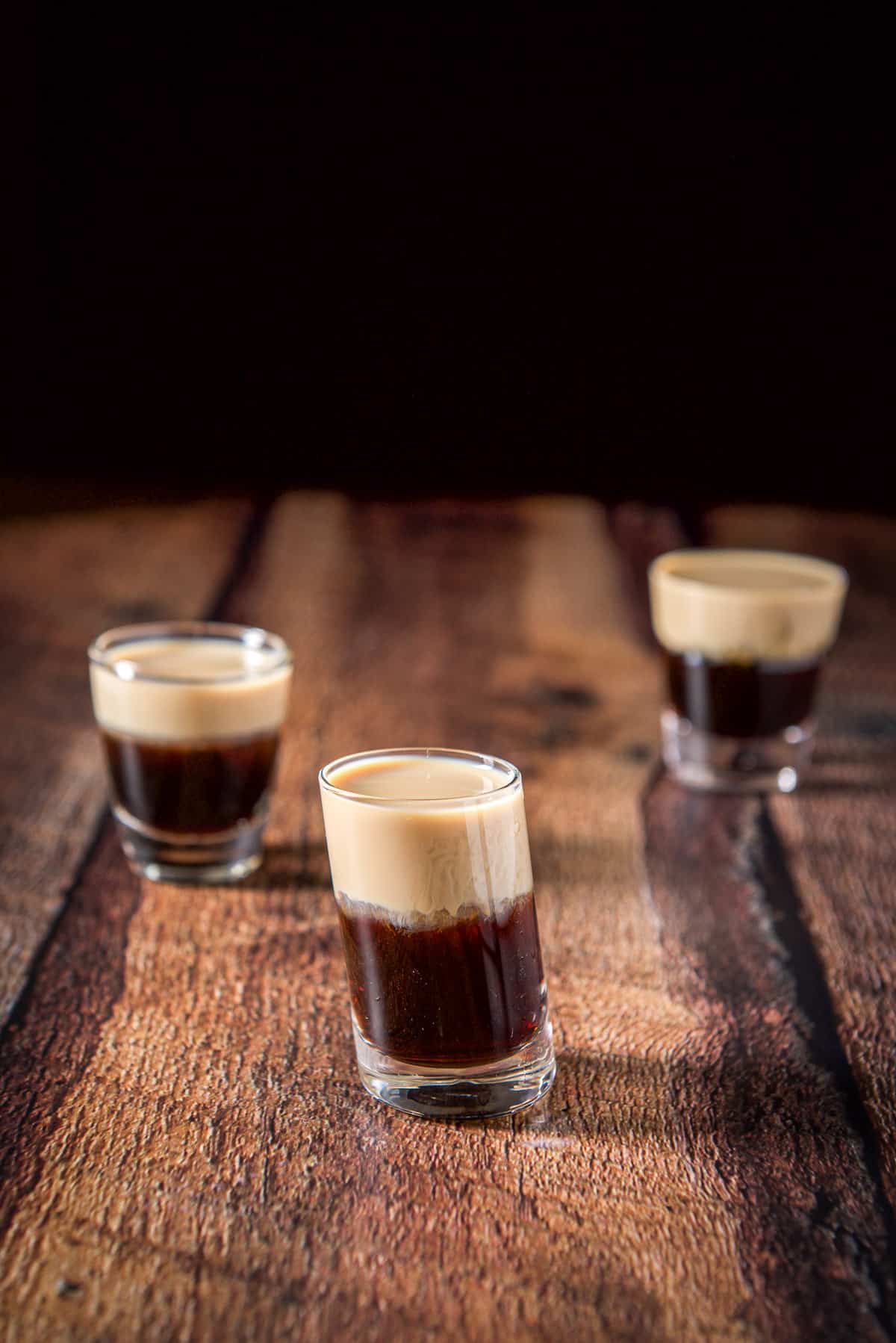 The tilted glass with the shot in front of the other two glasses - all on a wooden table
