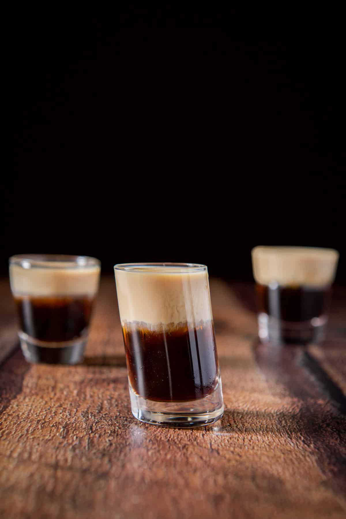 Vertical view of the tilted glass in front of the other two glasses all filled with the layered shot