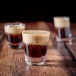 Three glasses with the layered shot in it with the beveled glass in the front