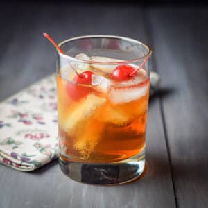 A double old fashioned glass filled with the Manhattan with two cherries in it - square