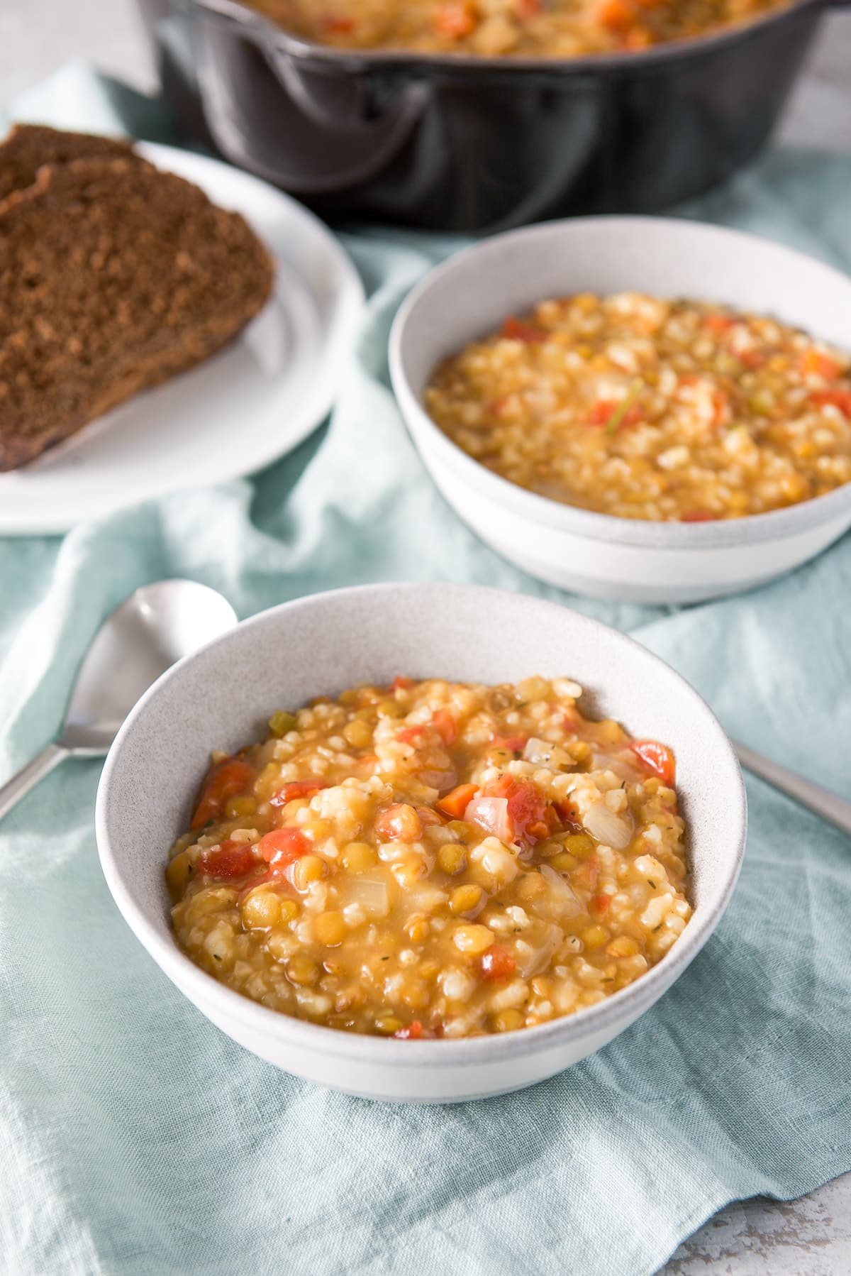 Two grey bowls filled with the thick soup with some bread and the pan behind them