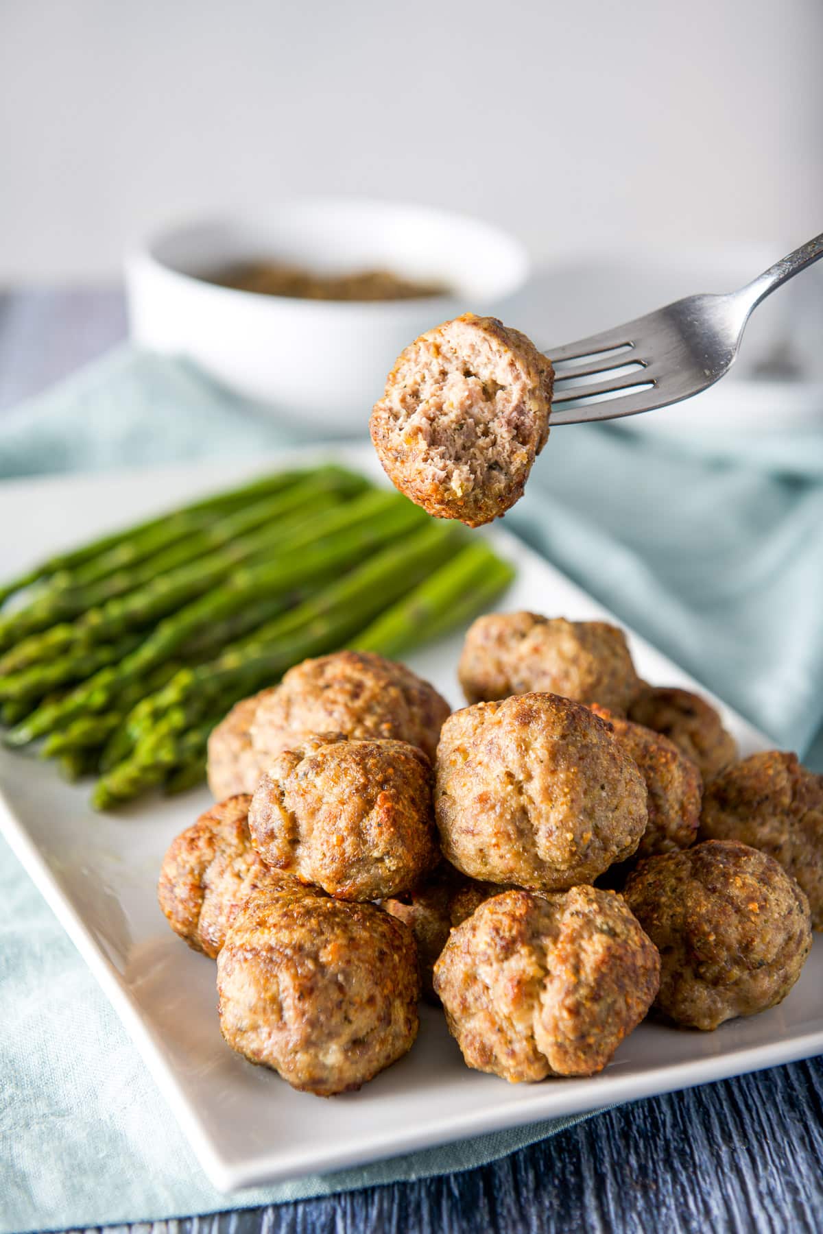 A fork holding a meatball with a bite taken out of it over the platter with meatballs under it