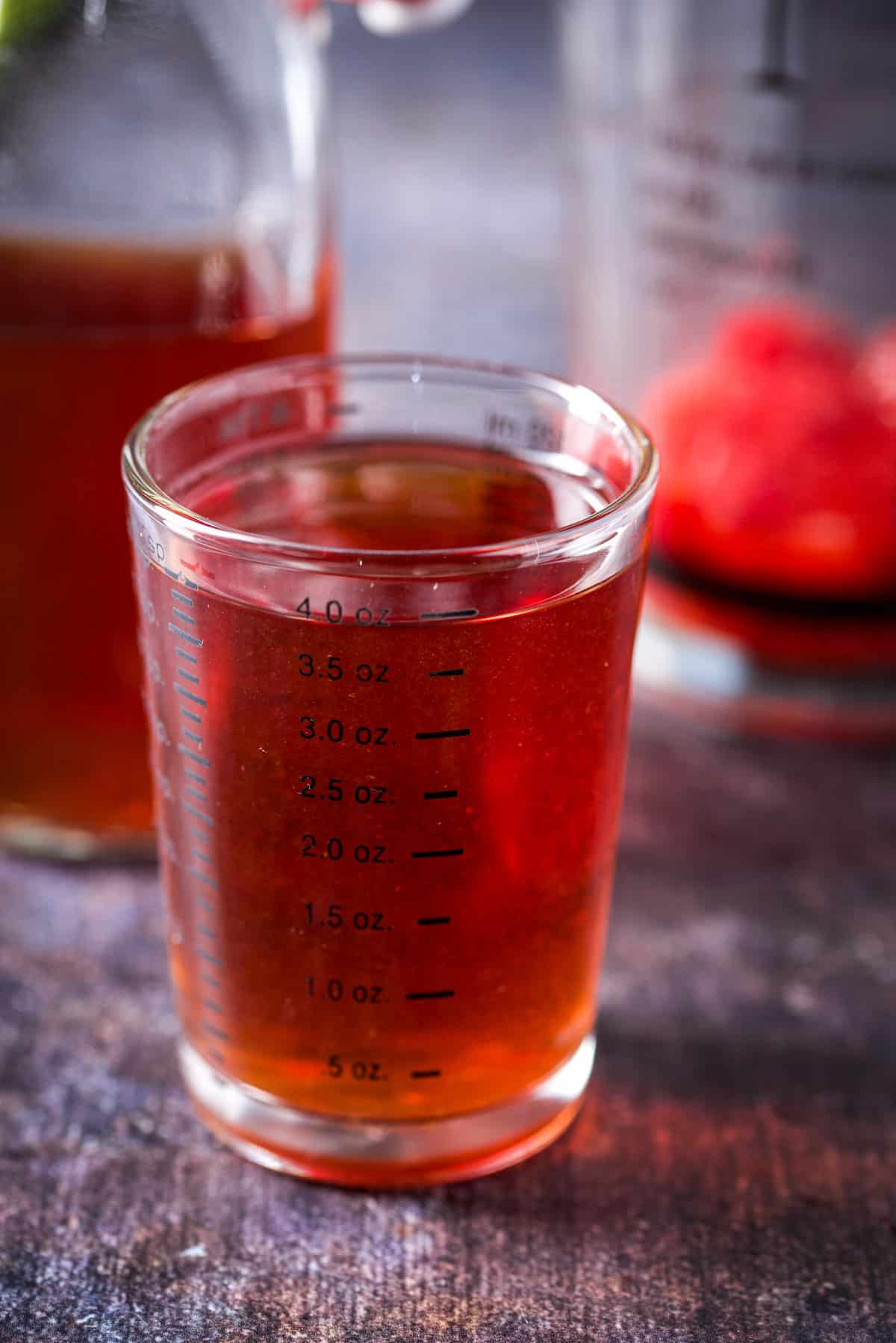 Strawberry vodka measured out with the bottle and shaker in the back