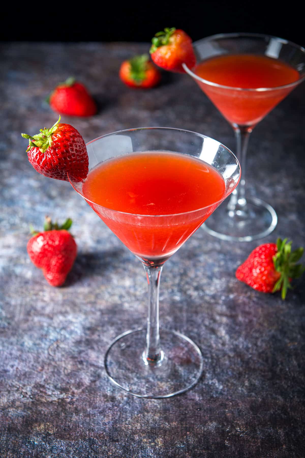 Two martini glasses filled with the strawberry cocktail with the fruit on the rims and table