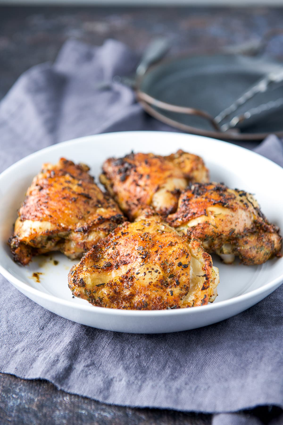 four cooked chicken thighs in a white deep dish with a metal plate behind it