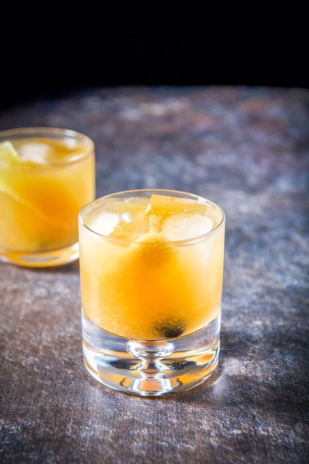 A thick glass in front of a double old fashioned glass filled with the amaretto cocktail
