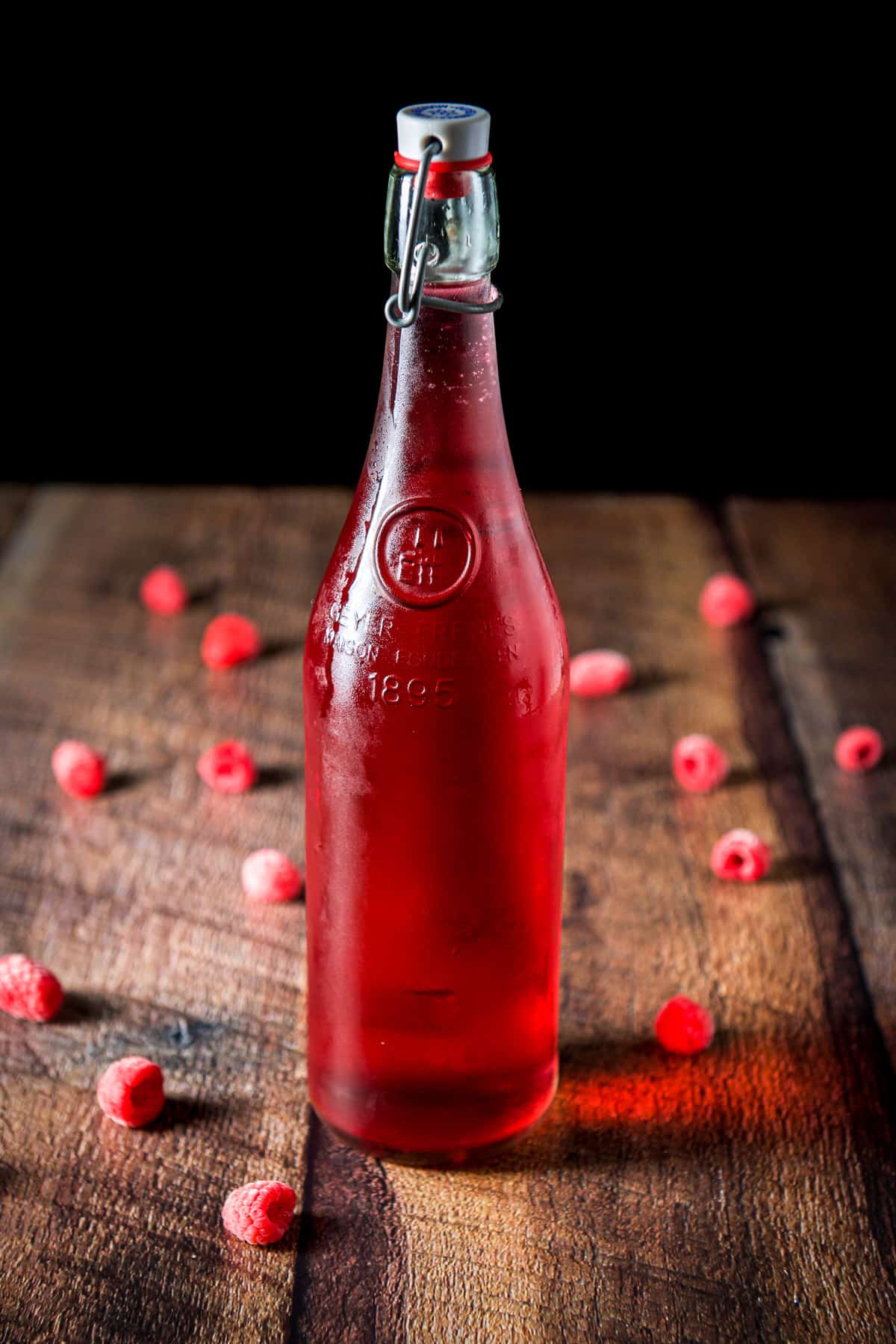 A capped bottle of red vodka with raspberries on the table