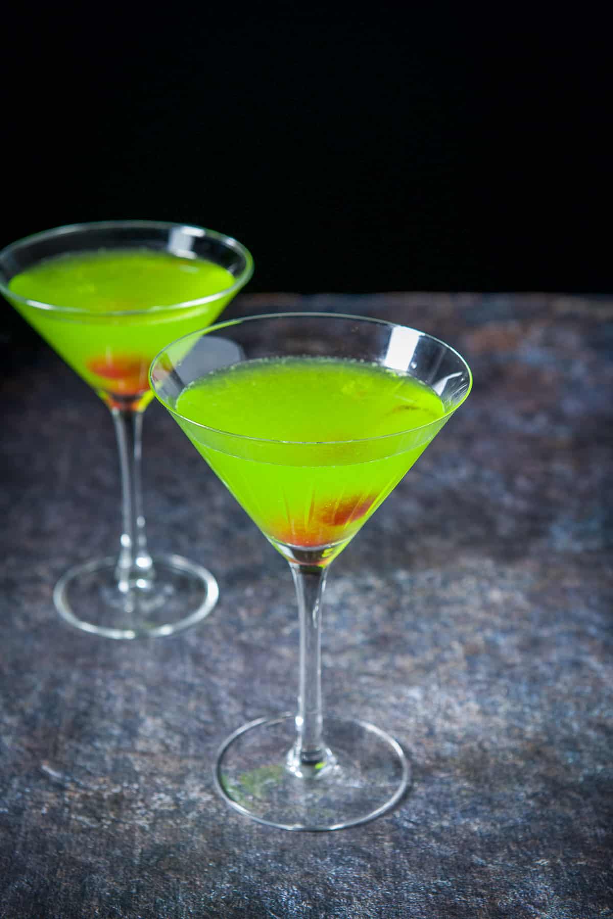Midori cocktail in two martini glasses with cherry garnish