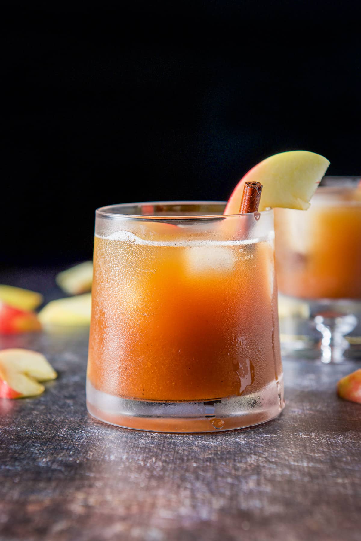 A sloped glass with the apple cocktail in it with an apple slices and cinnamon stick