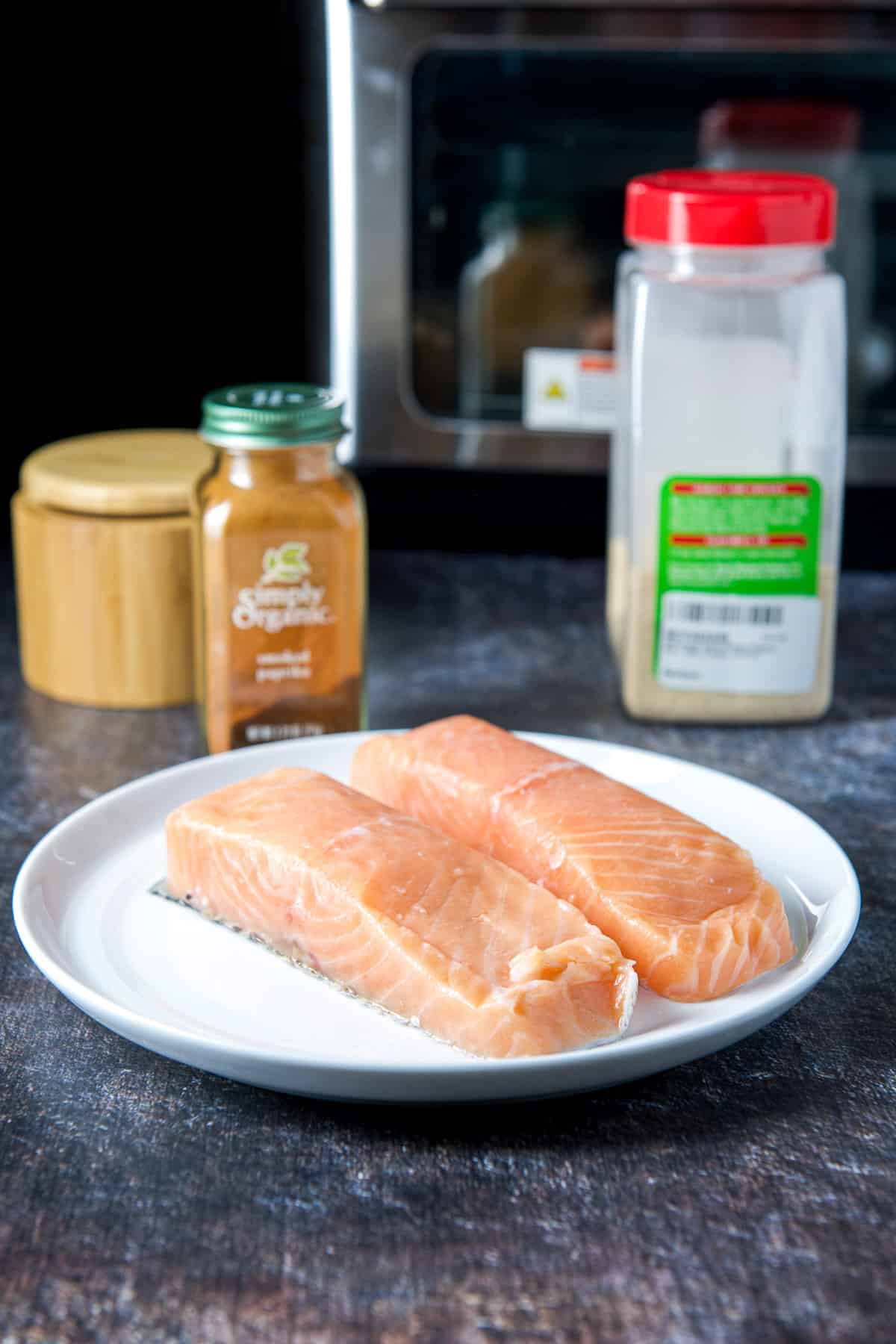 A white plate with two thin pieces of salmon, salt, garlic powder and smoked paprika