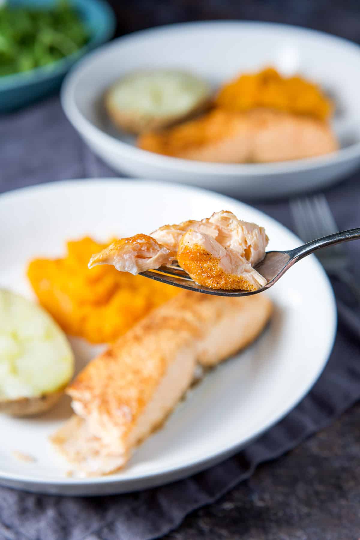 A bite of salmon on a fork held over the plate with the meal on it