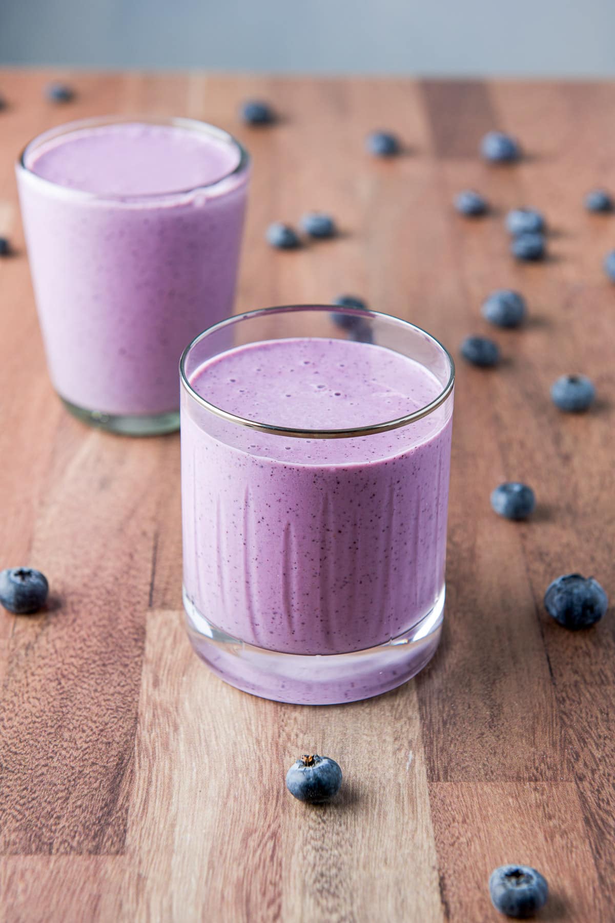 Two glasses filled with the blue smoothie and blueberries on the table