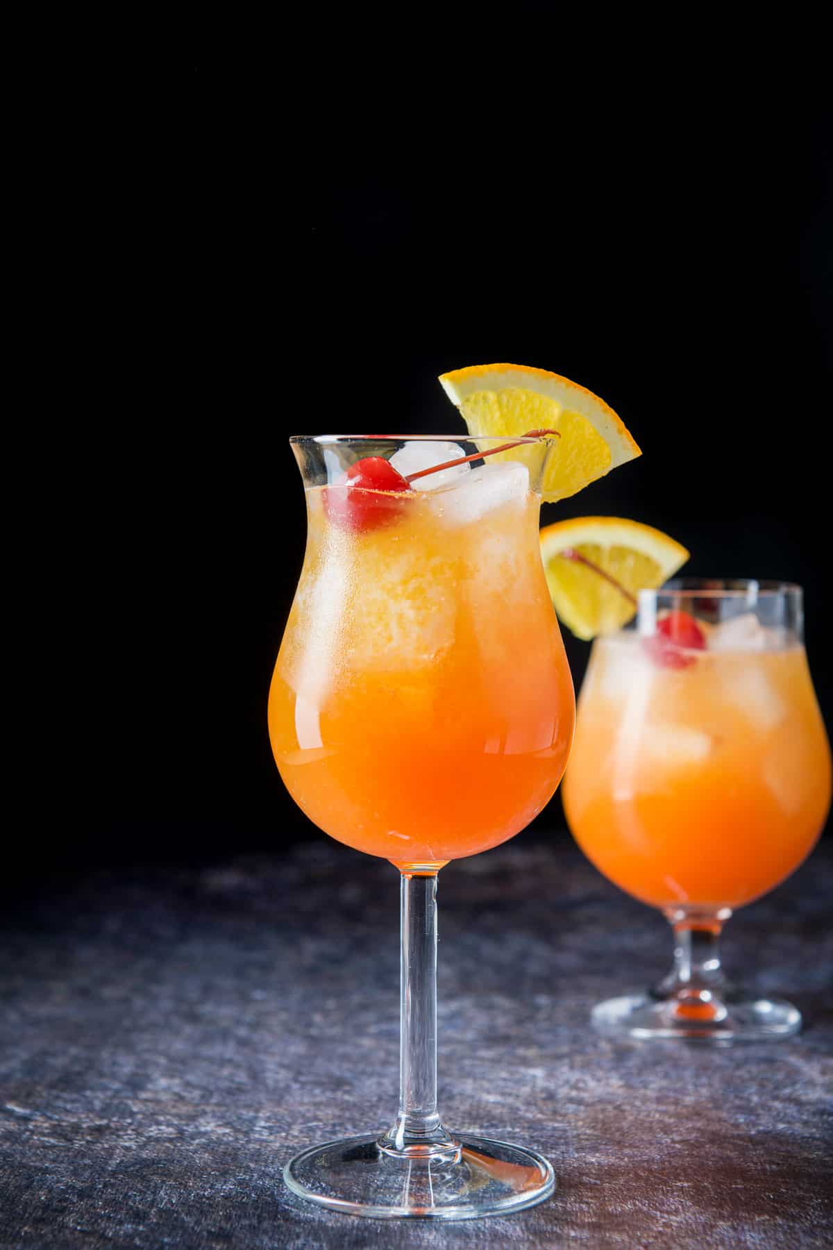 Vertical view of the tall tulip glass in front of the shorter glass filled with the orange red cocktail