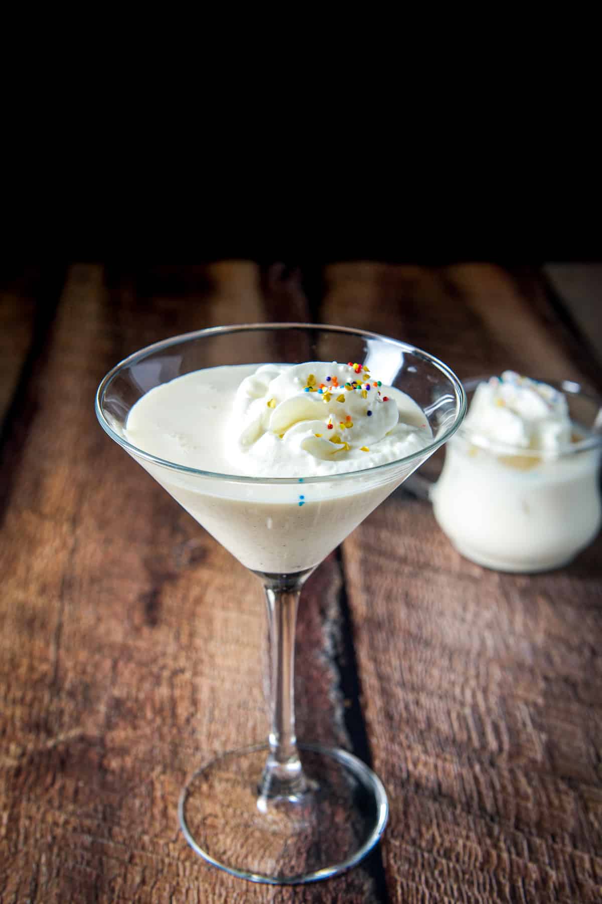 Two glasses - a classic martini and a smaller glass filled with the creamy cocktail with whipped cream and sprinkles