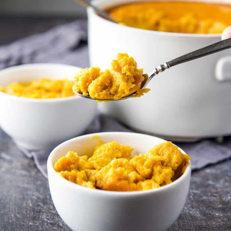 A spoonful of souffle held over a small bowl if it with the big bowl in the back