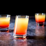 Tilted glass in front of two other glasses filled with the pineapple upside down shot