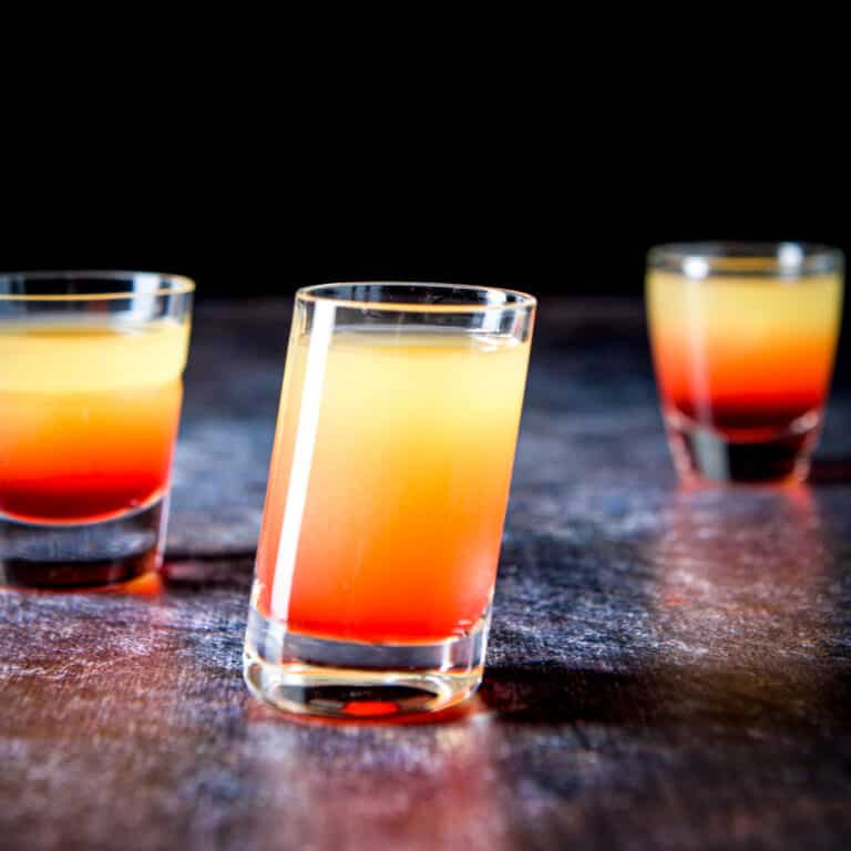 Tilted glass in front of two other glasses filled with the pineapple upside down shot