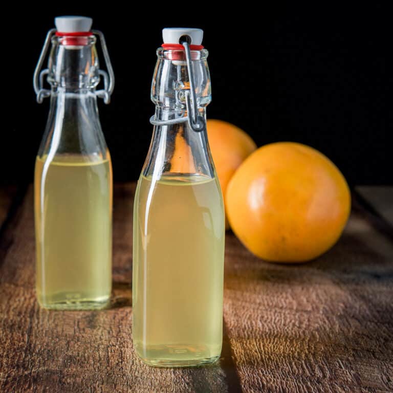 Square photo of two bottles of infused vodka with two grapefruit behind it