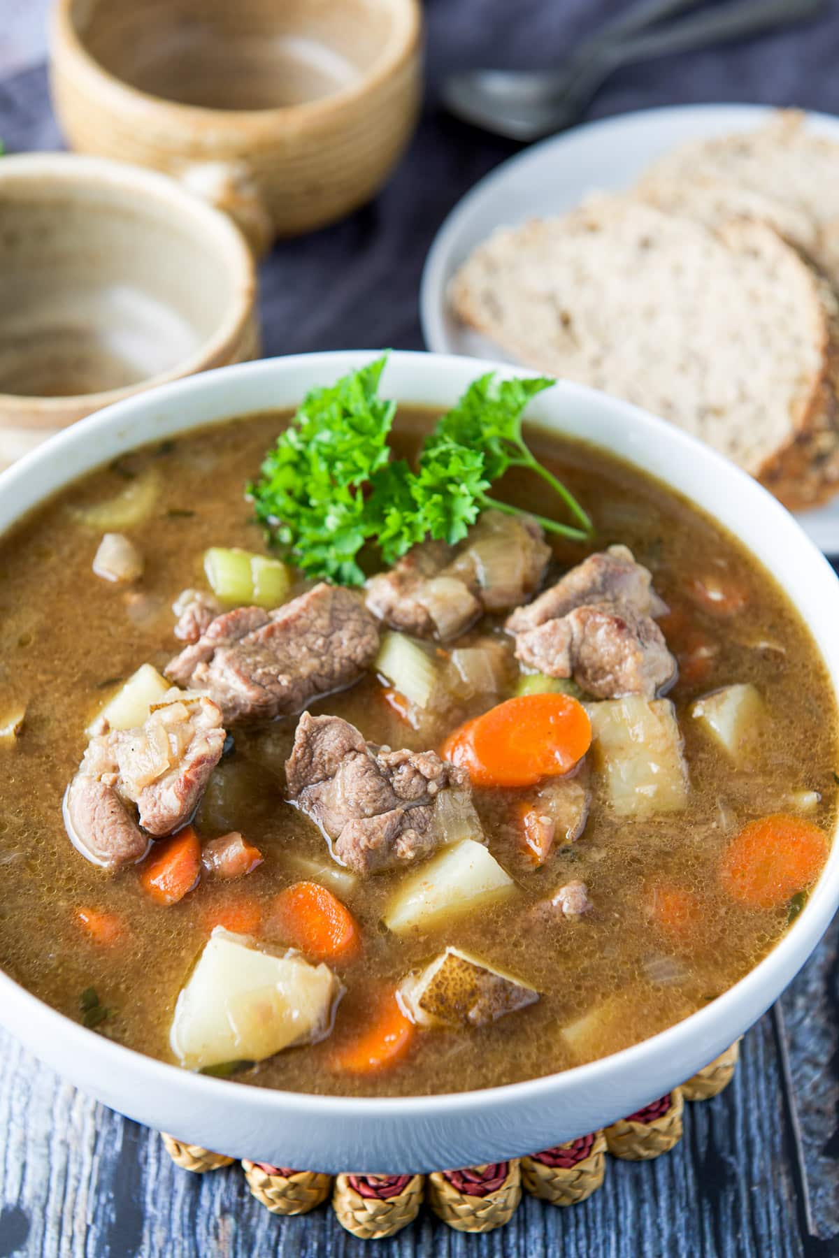 A big white bowl filled with a hearty stew with crocks and bread in the back