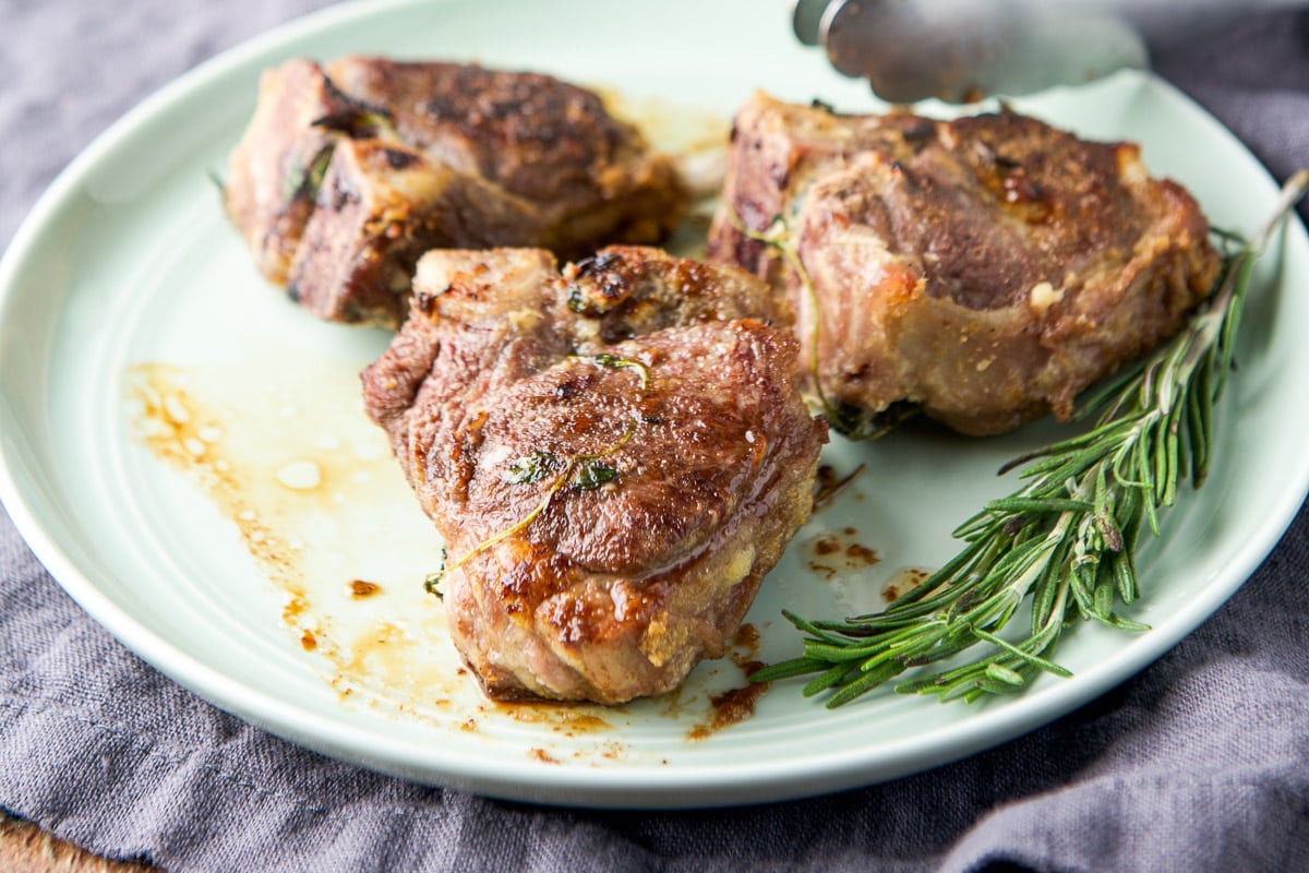 Three lamb chops on a green plate with fresh rosemary - horizontal