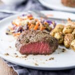A white plate with a steak with a cut in it, with potatoes and veggies - square