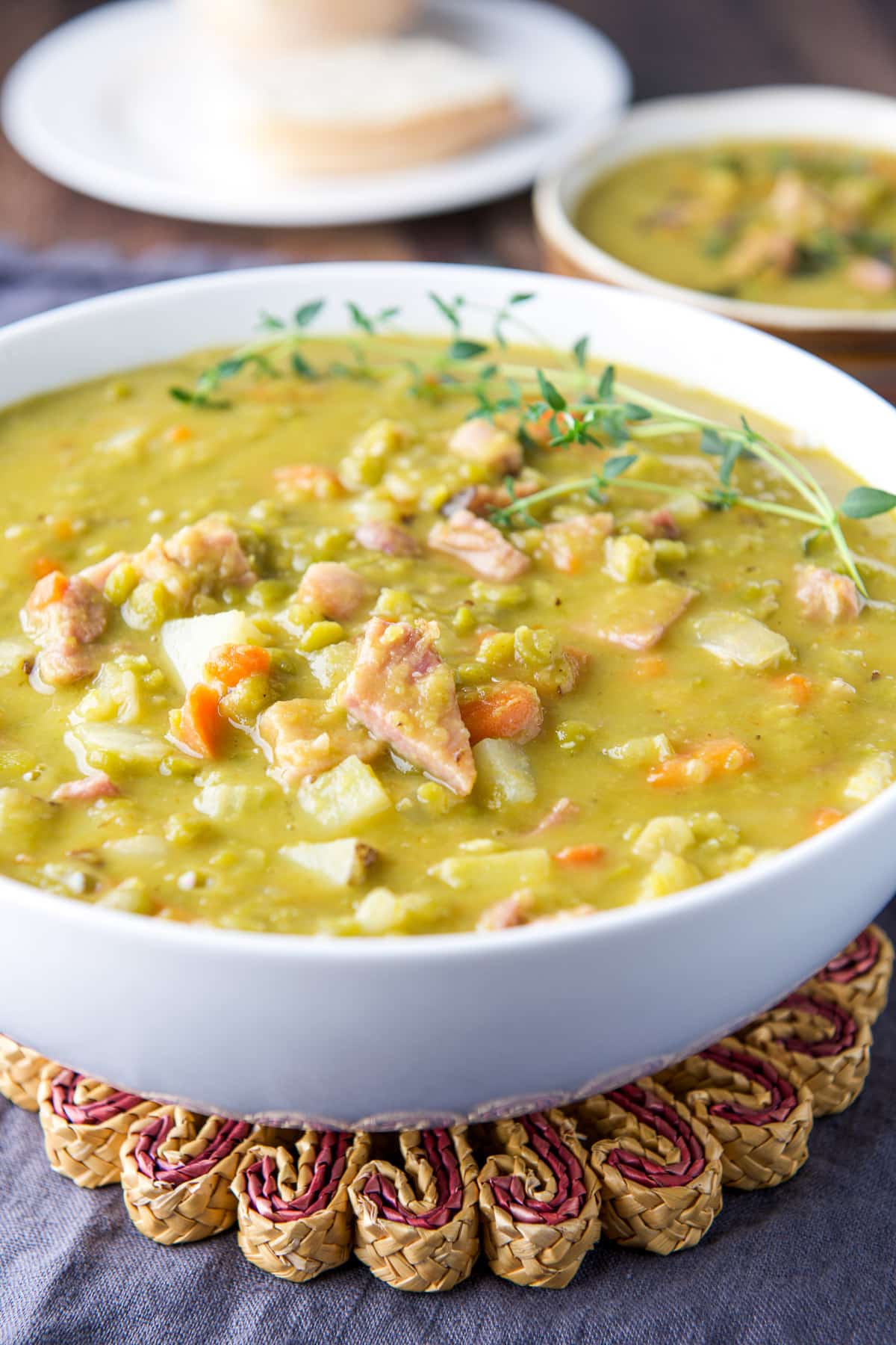 A white bowl filled with the ham and pea soup with more in the back along with bread