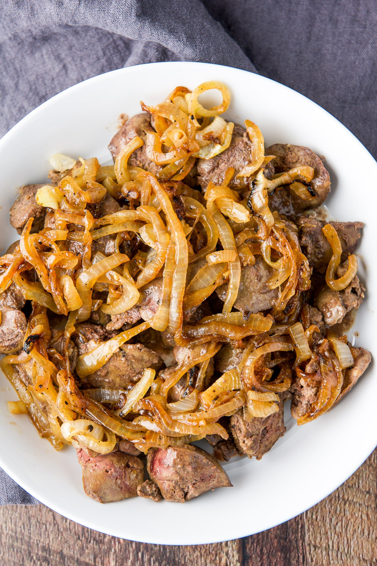 Overhead view of a white plate of chicken livers with onions on top