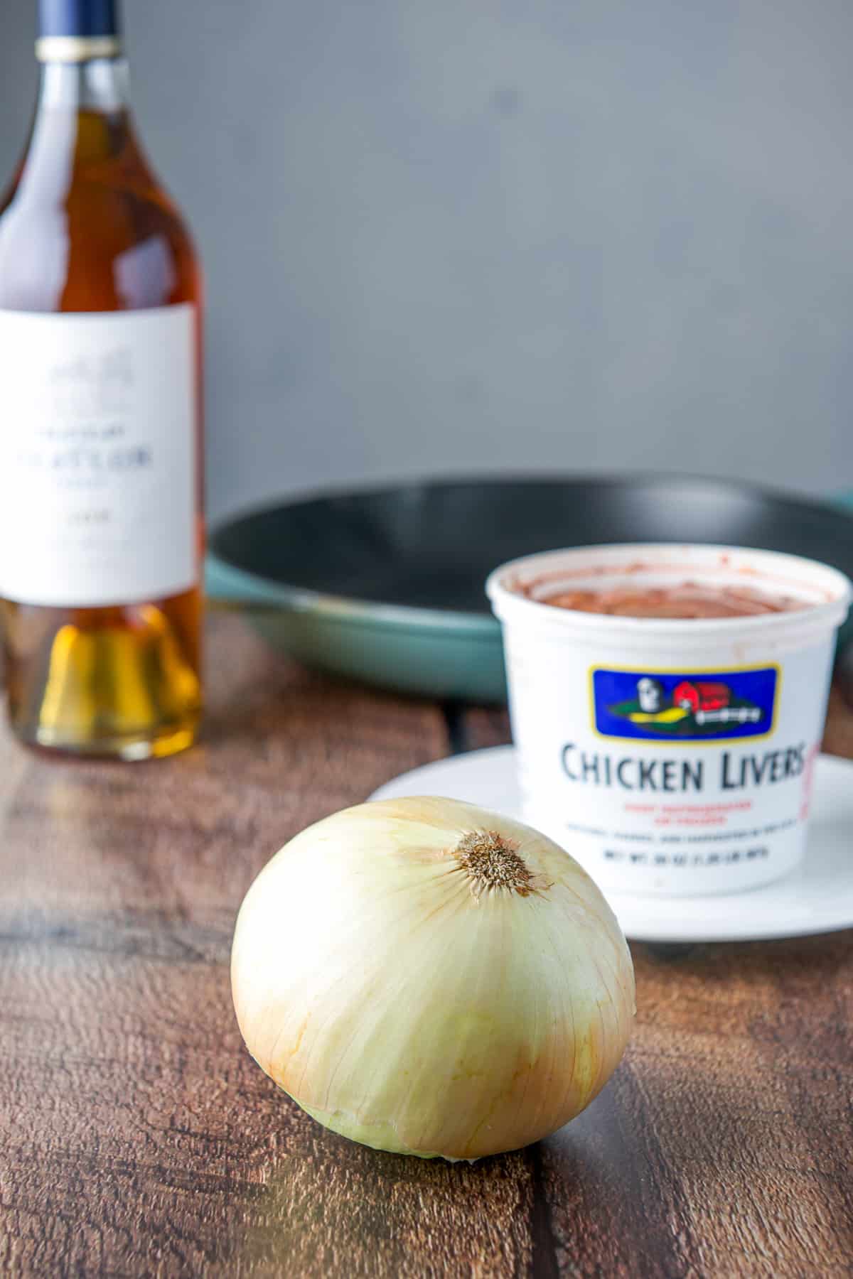 Onion, livers, cognac and a pan on a table.