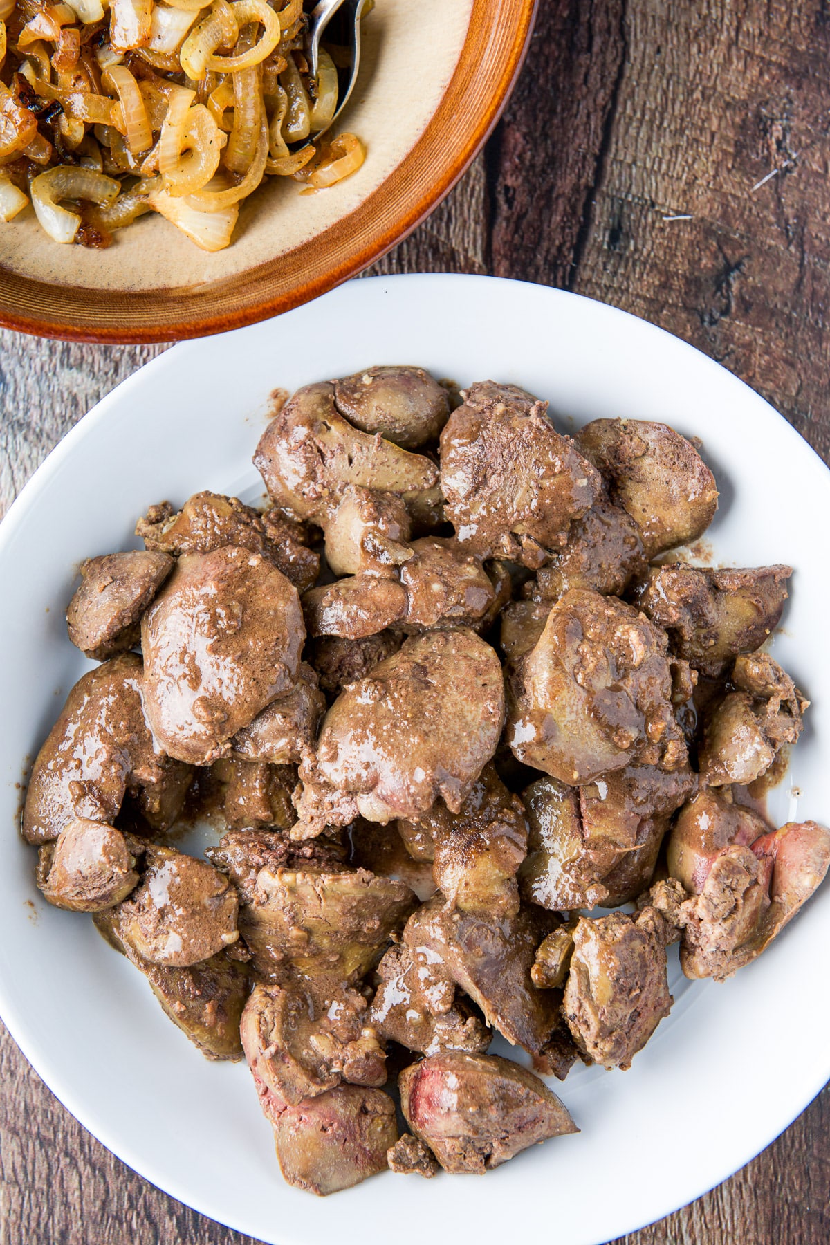 Overhead view of a white plate of livers and bowl of onions