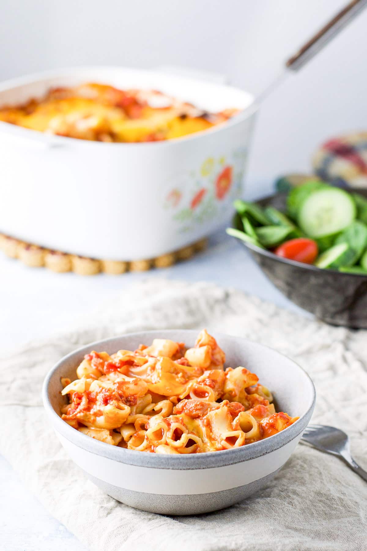 A grey bowl with pasta in it with the casserole dish in the back