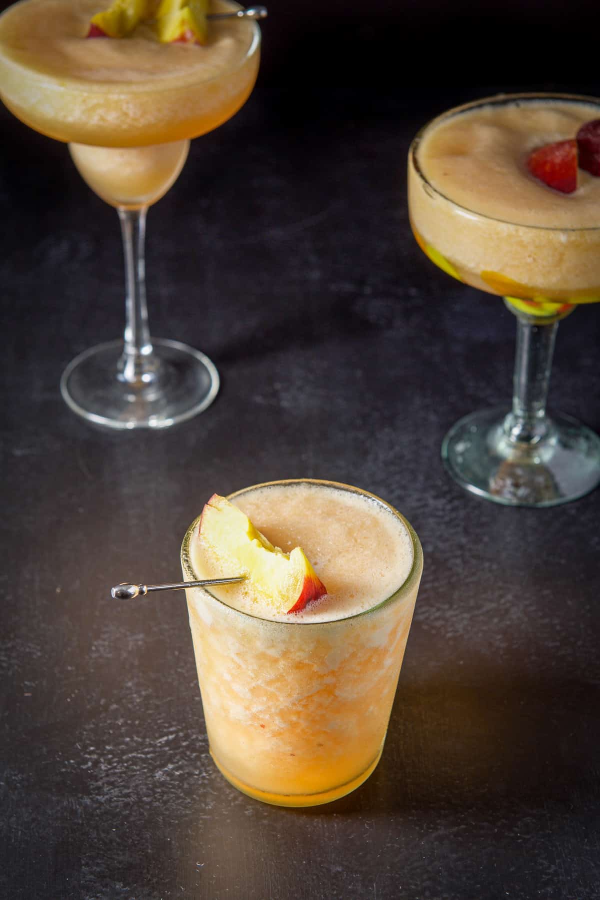A highball glass filled with the frozen margarita with fresh peach slices as garnish