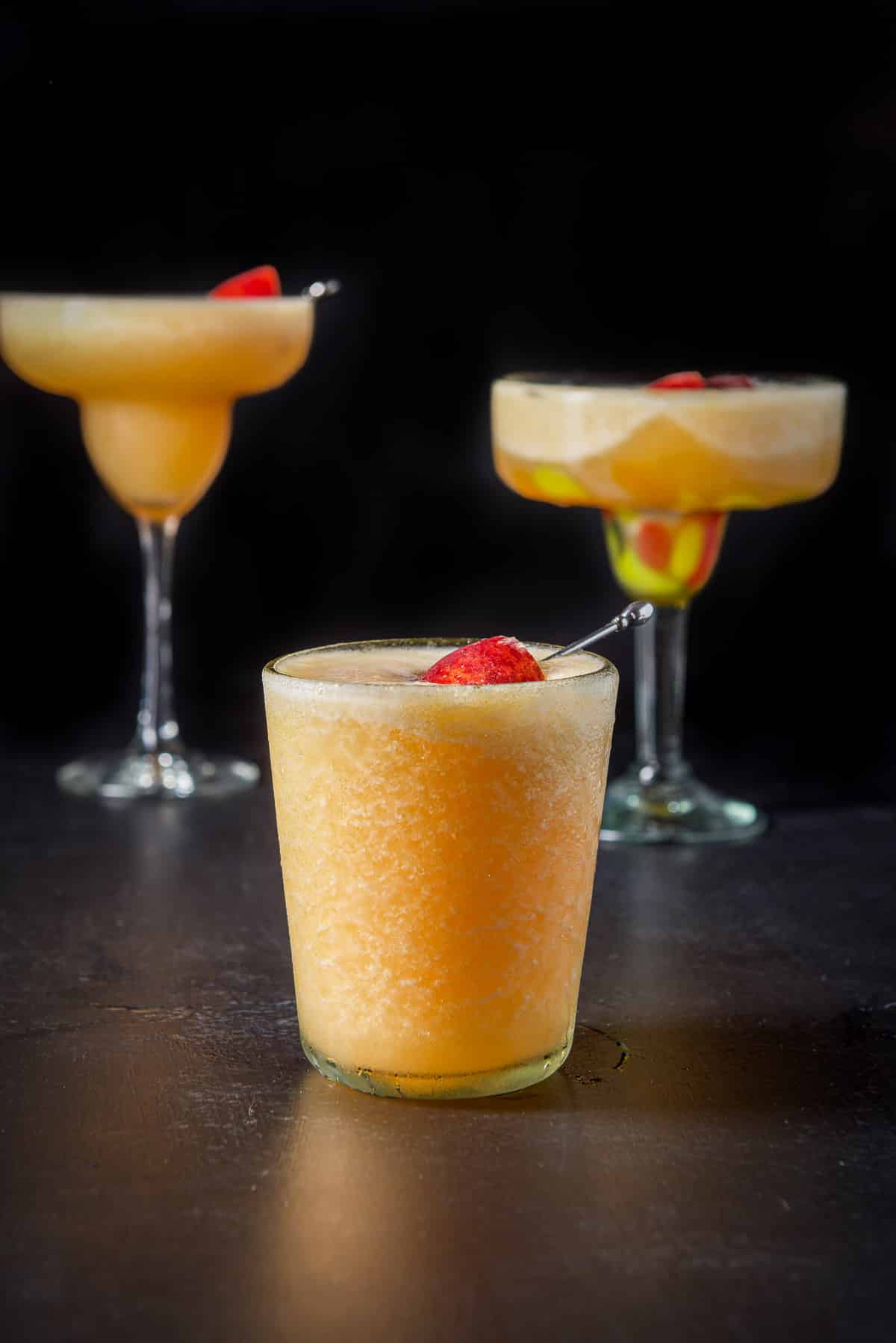 Double old fashioned glass filled with the peach margarita with the other two glasses behind it