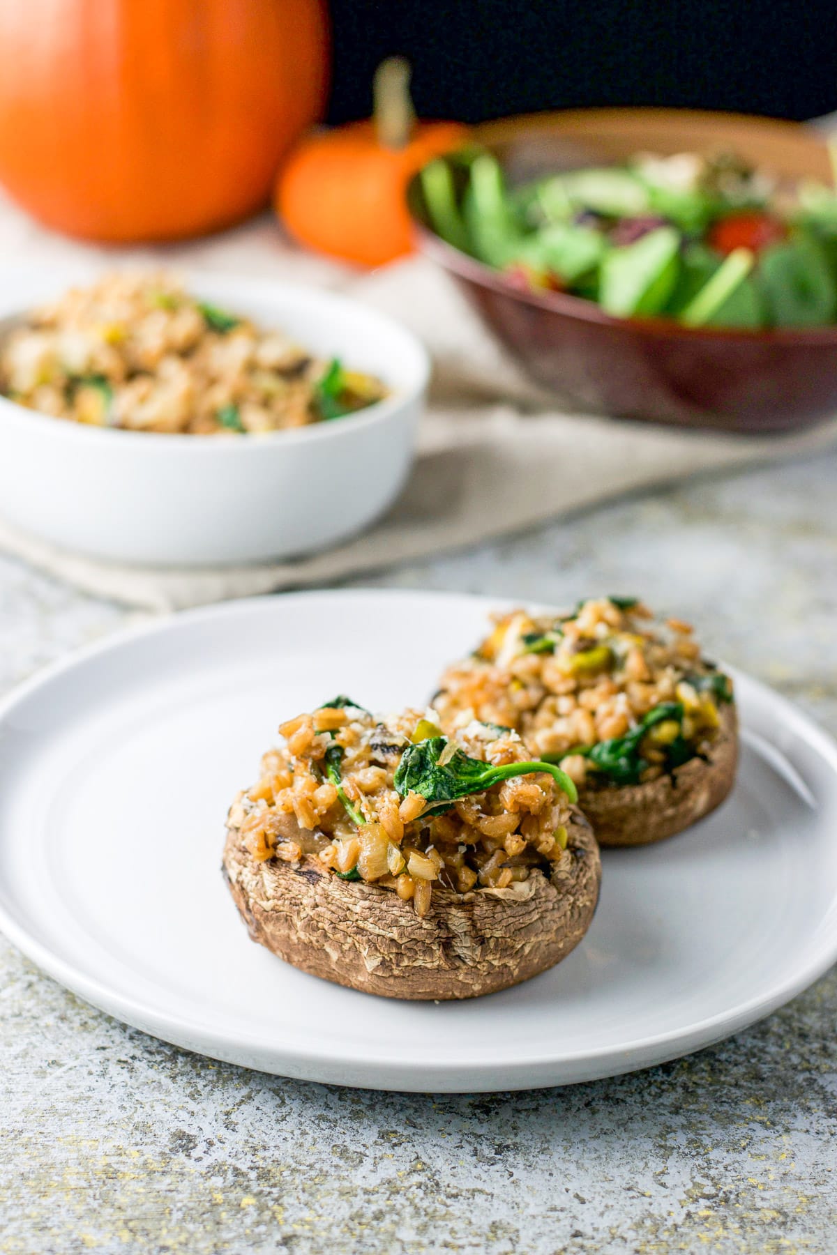 A plate with two stuffed mushroom caps on it with a salad and stuffing in back