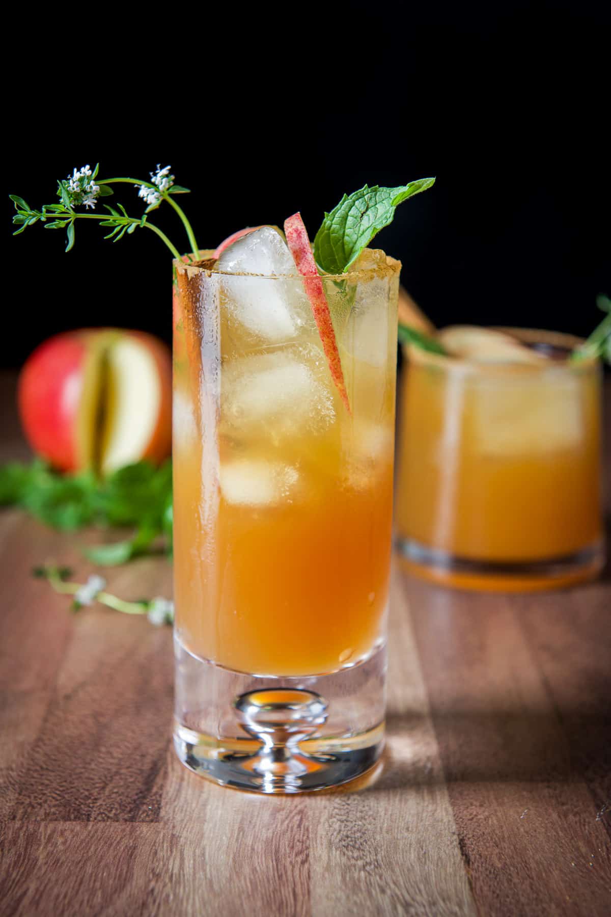 Two glasses filled with the spritzer with mint, thyme and apple slices as garnish