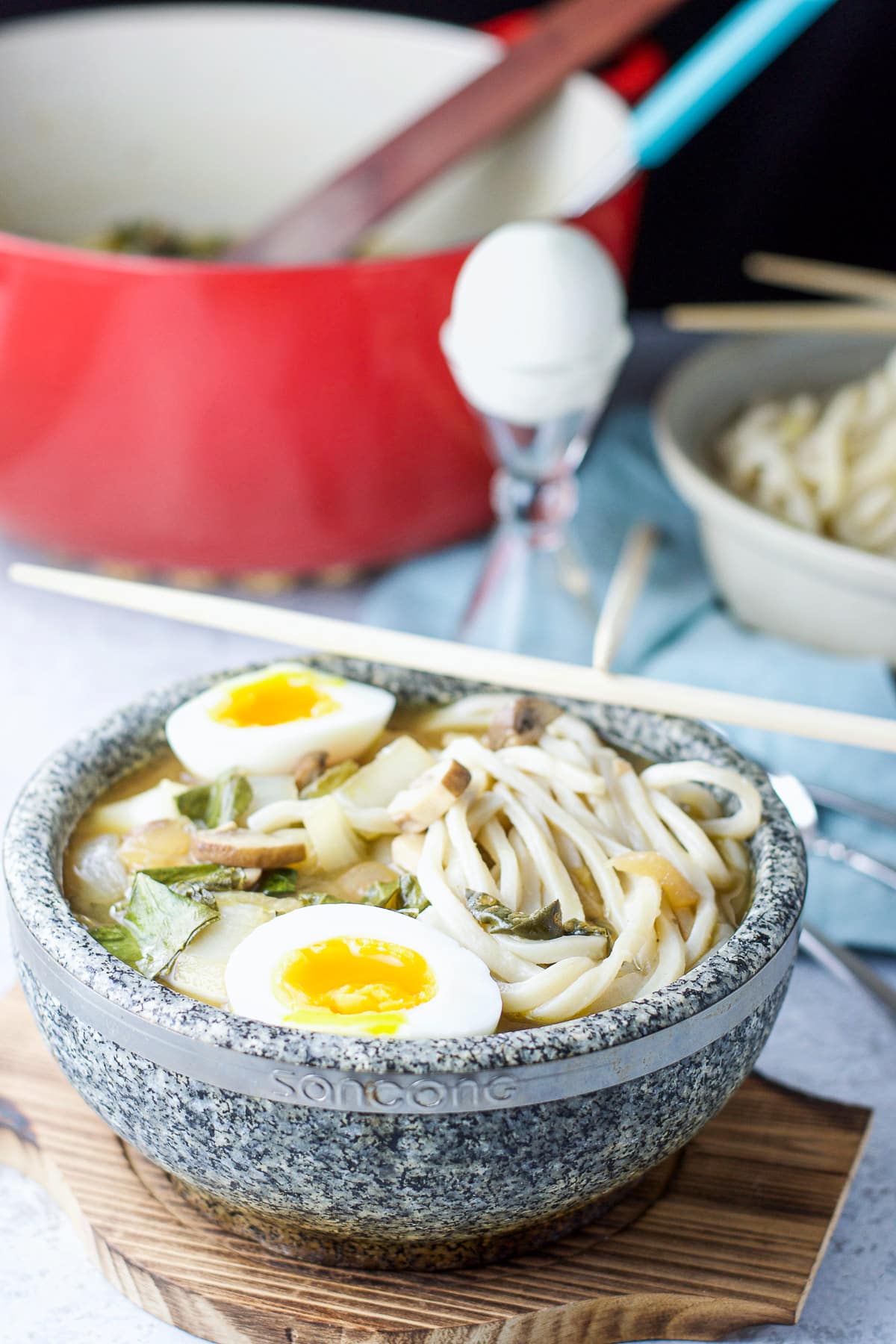 Stone bowl with the soup with noodles, egg and pan in the back