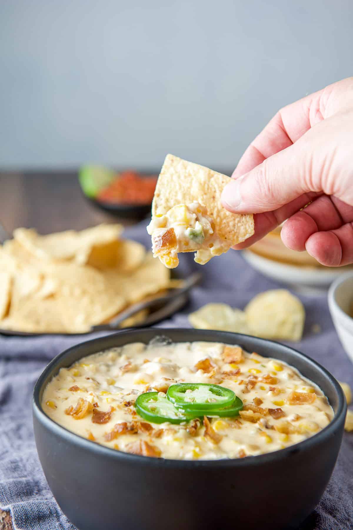 A hand holding a corn chip with the dip on it