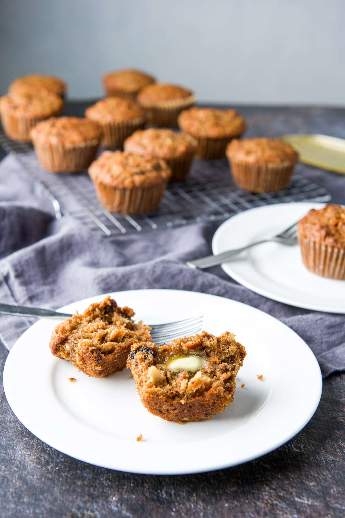 A muffin torn in half with butter on one half with more muffins in the back