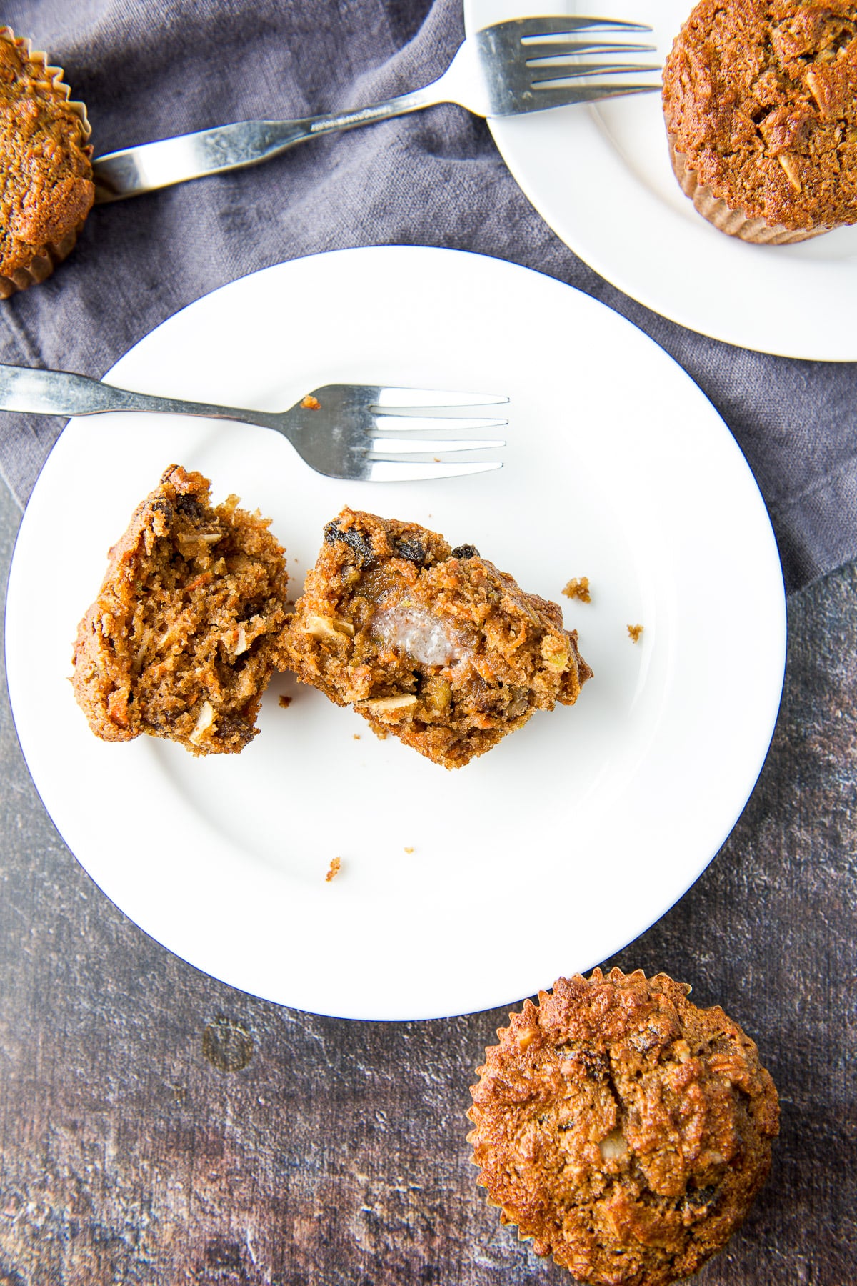 Overhead view of a white plate with a muffin torn in half with muffins off to the sides