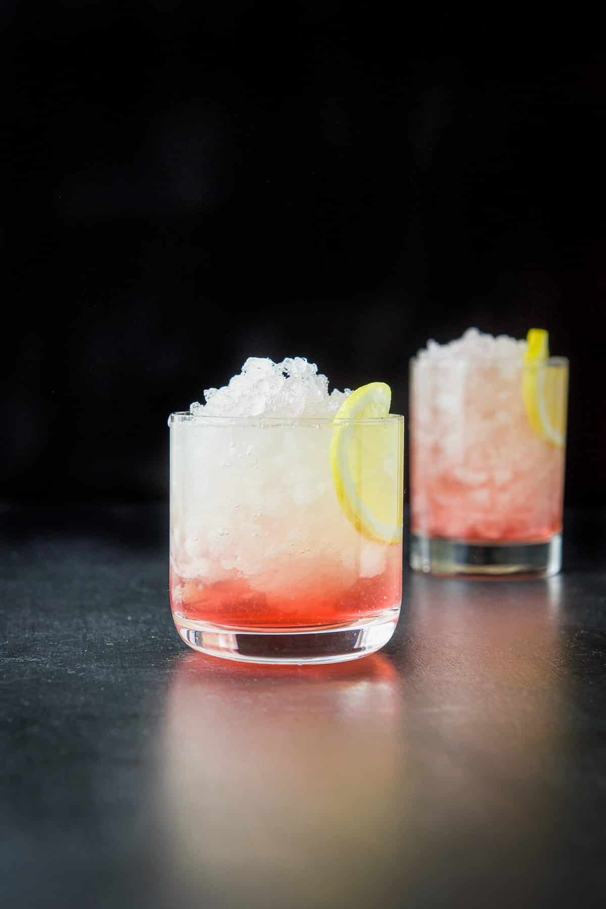 Vertical view of two glasses filled with the bramble cocktail with lemon as garnish