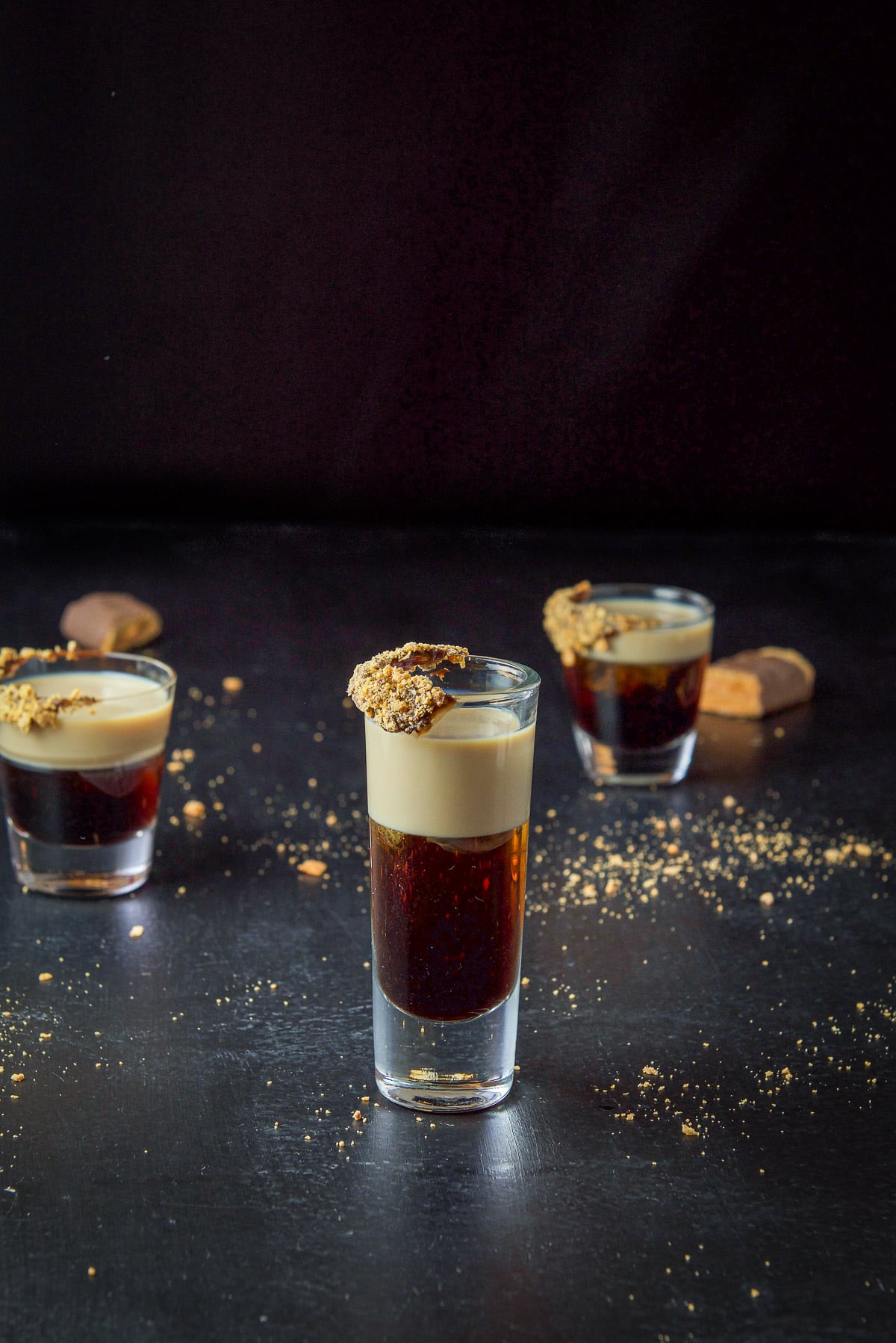 Tall thin glass with the layered shot in it with more glasses and butterfinger bars on the table