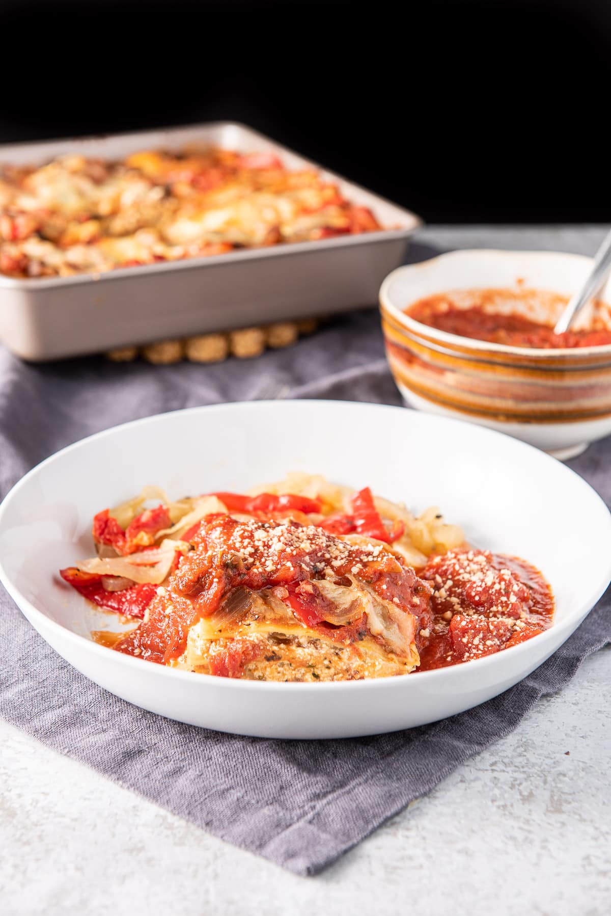 A white plate with lasagna on it with the pan of it behind