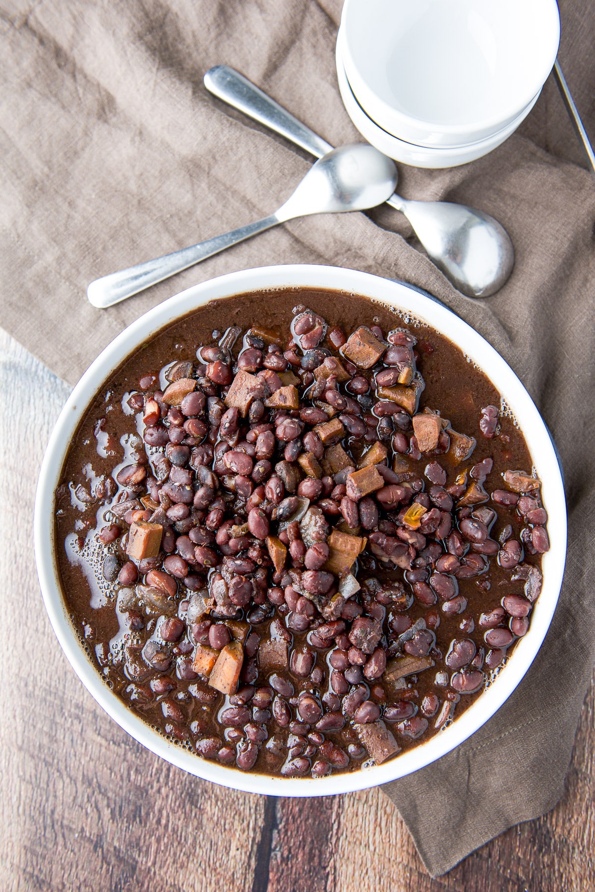 Overhead view of black beans in a big bowl with spoons and small bowls