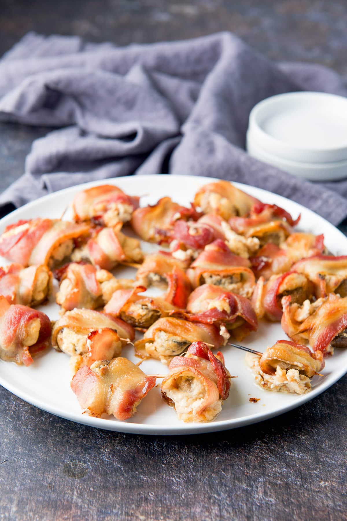 mushrooms wrapped in bacon on a white plate with smaller plates in back