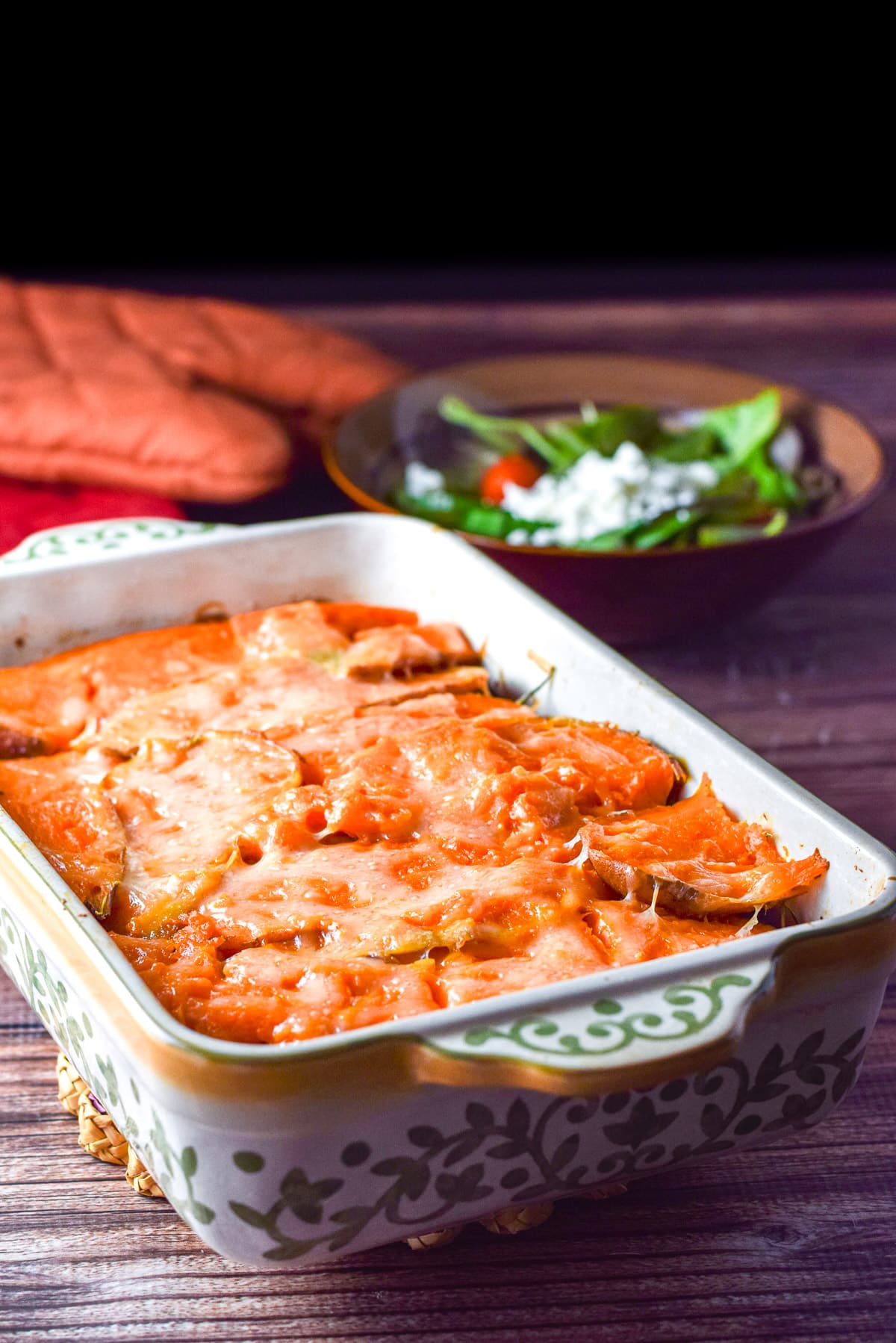 A casserole dish with the cooked shepherds pie and a salad in the back