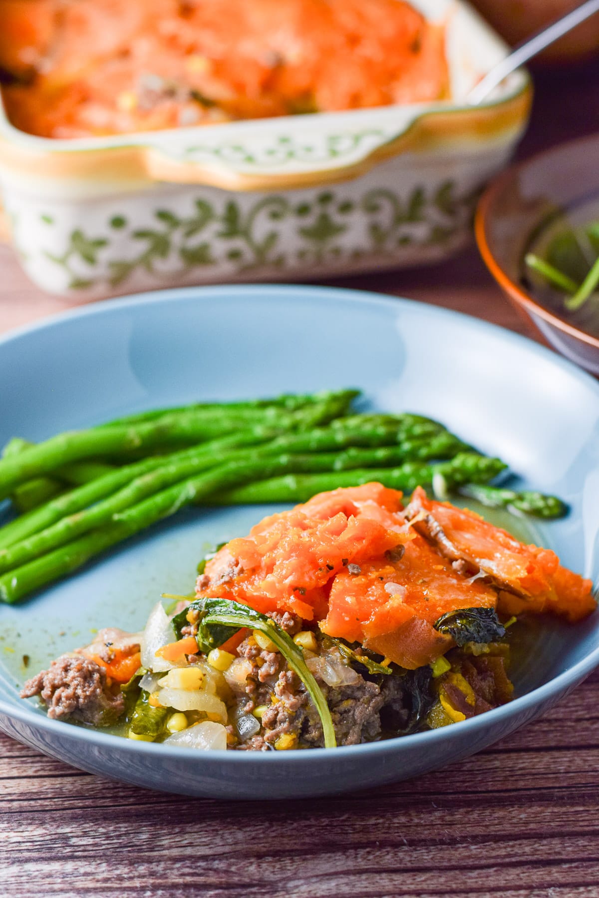 A blue plate with the piece of meat pie on it with asparagus