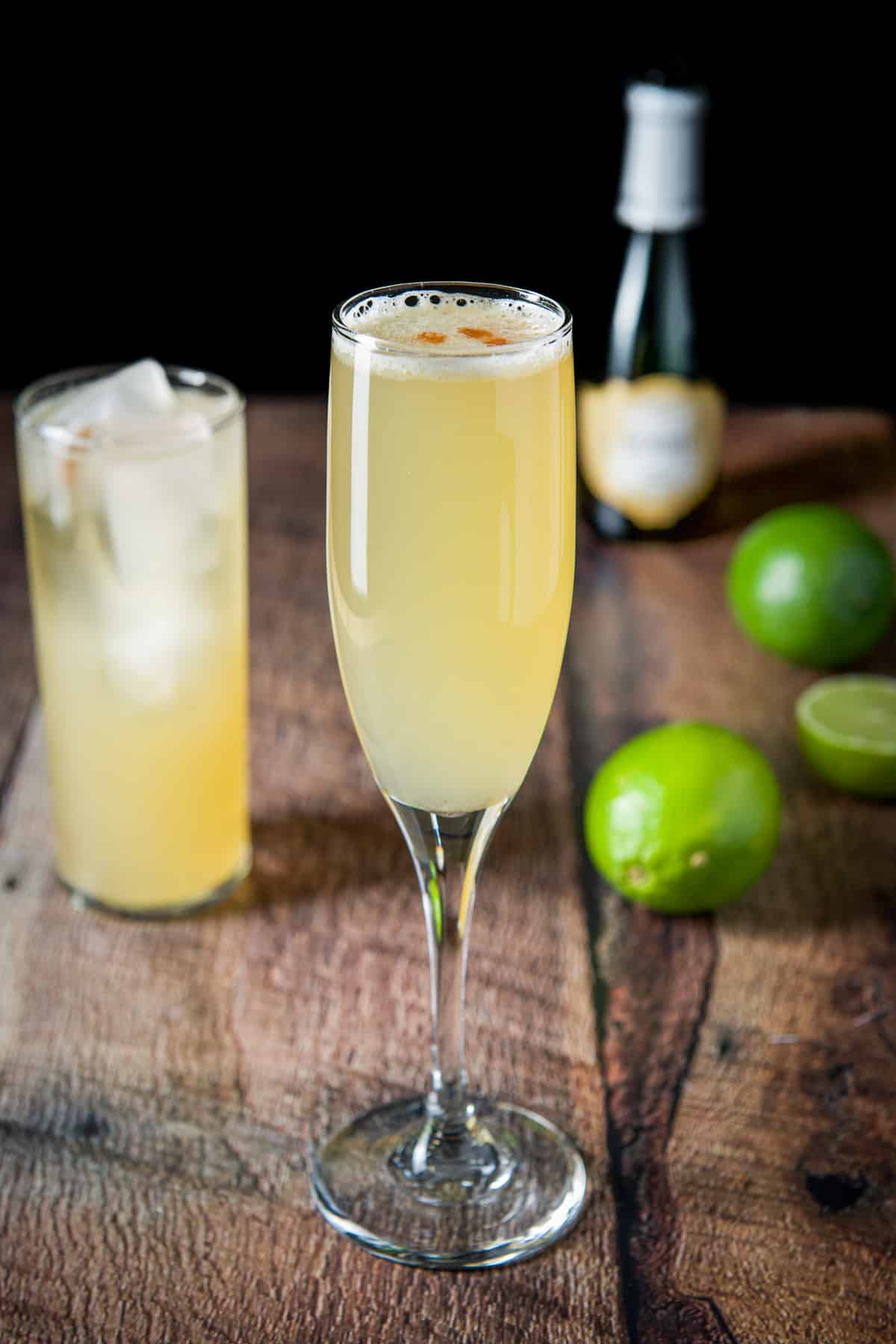 A champagne flute and tall glass filled with the airmail cocktail with limes on the table
