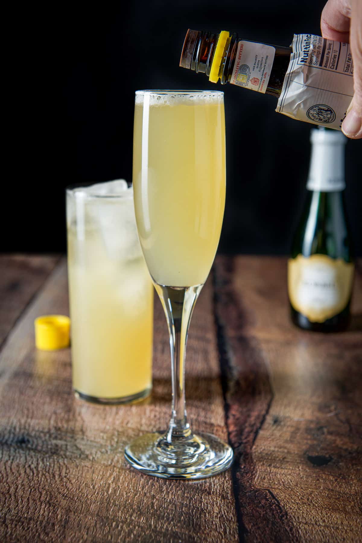 A hand holding the bitters bottle over the champagne flute