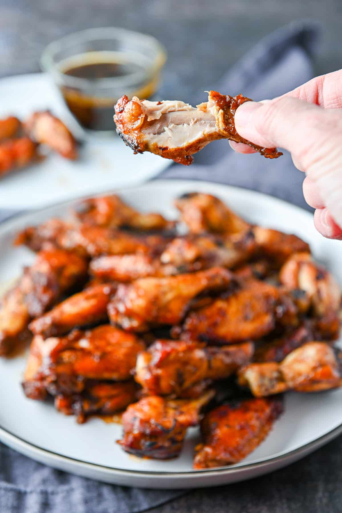 A hand holding a chicken wing with a bite out of it over the platter of wings