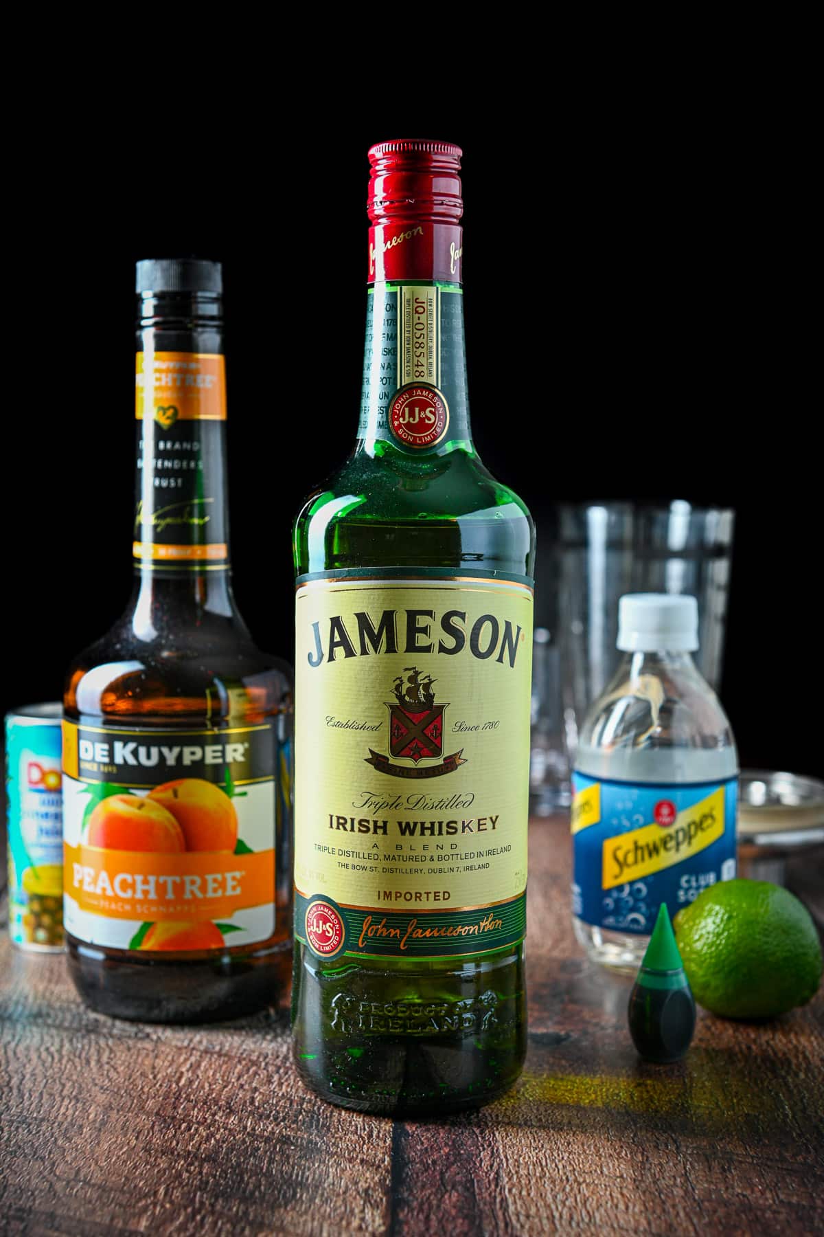 Whiskey, peach schnapp, pineapple juice, club soda, lime, and food coloring on a table